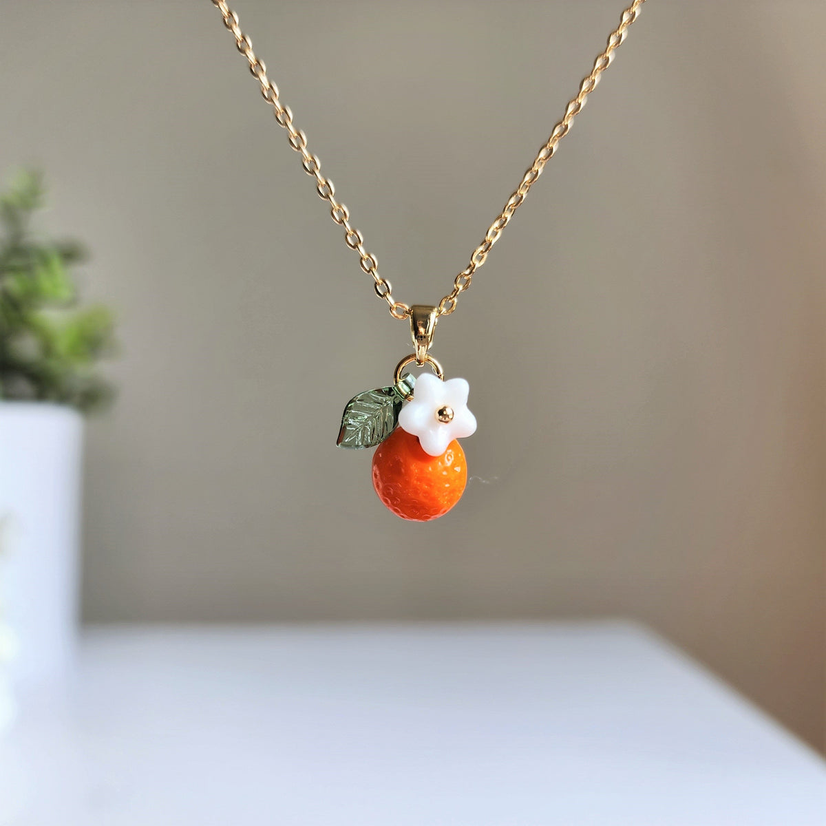 Gold-tone orange fruit charm necklace with white flower and green leaf, single charm