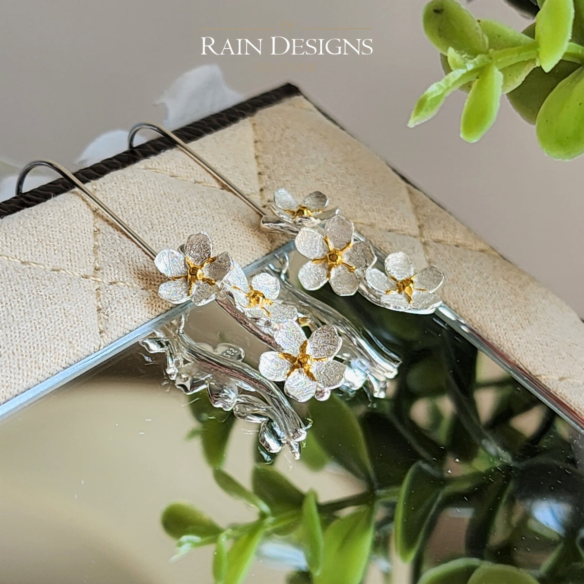 Silver flower hook earrings with small gold-accent blossoms, close-up