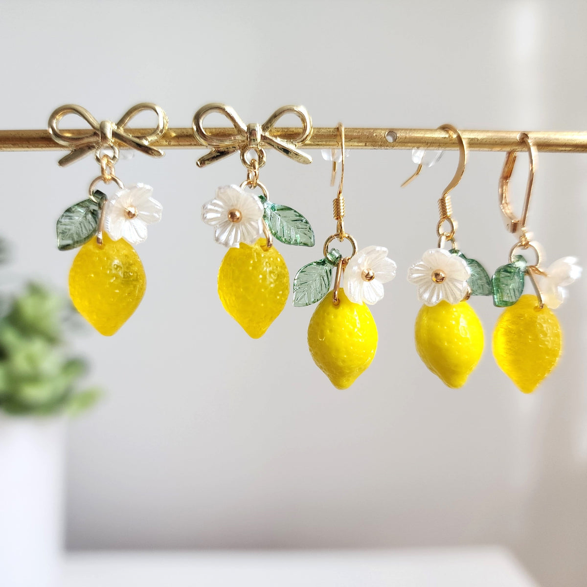 Close view of multiple lemon dangle earrings: yellow drops, green leaves, white flower charms