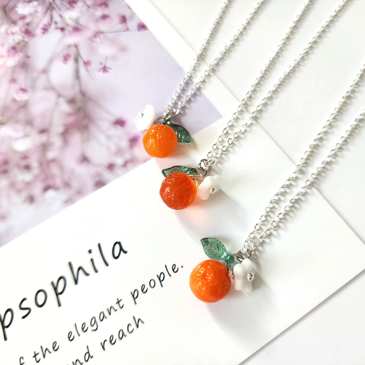 Silver-tone orange fruit charm necklace with white flower and green leaves