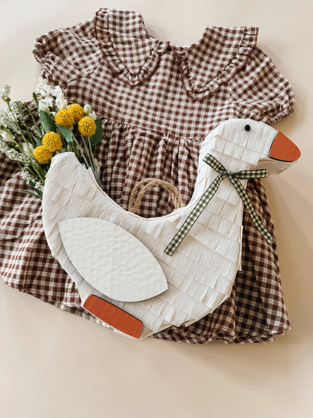 Goose piñata with white body, orange beak and feet, and green plaid bow