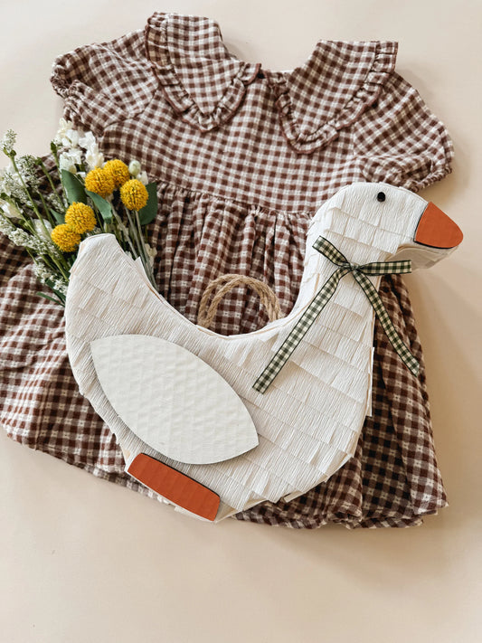 Goose piñata with white body, orange beak and feet, and green plaid bow