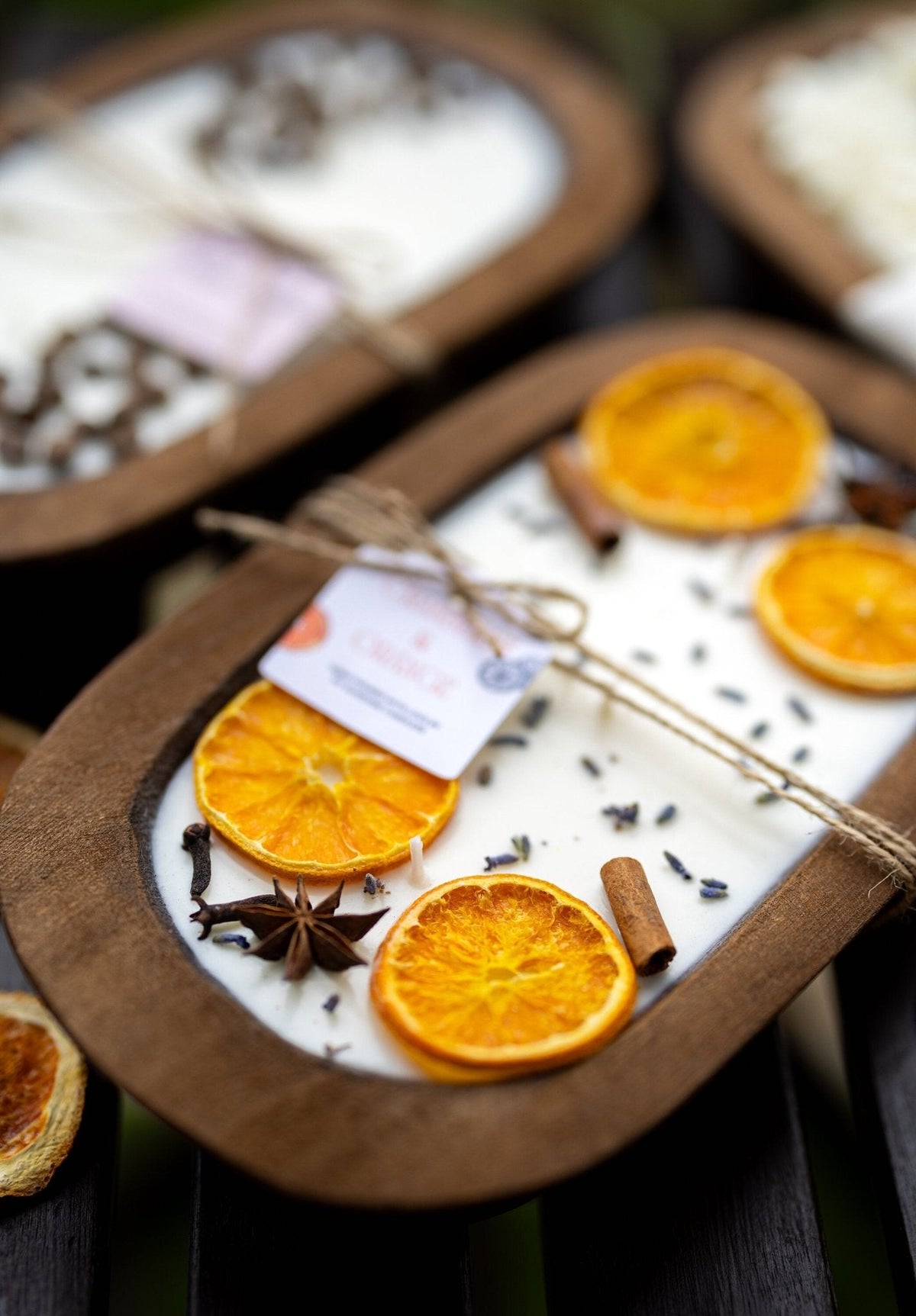Soy candle in wooden dough bowl with orange slices and spice seeds; scent card tied on