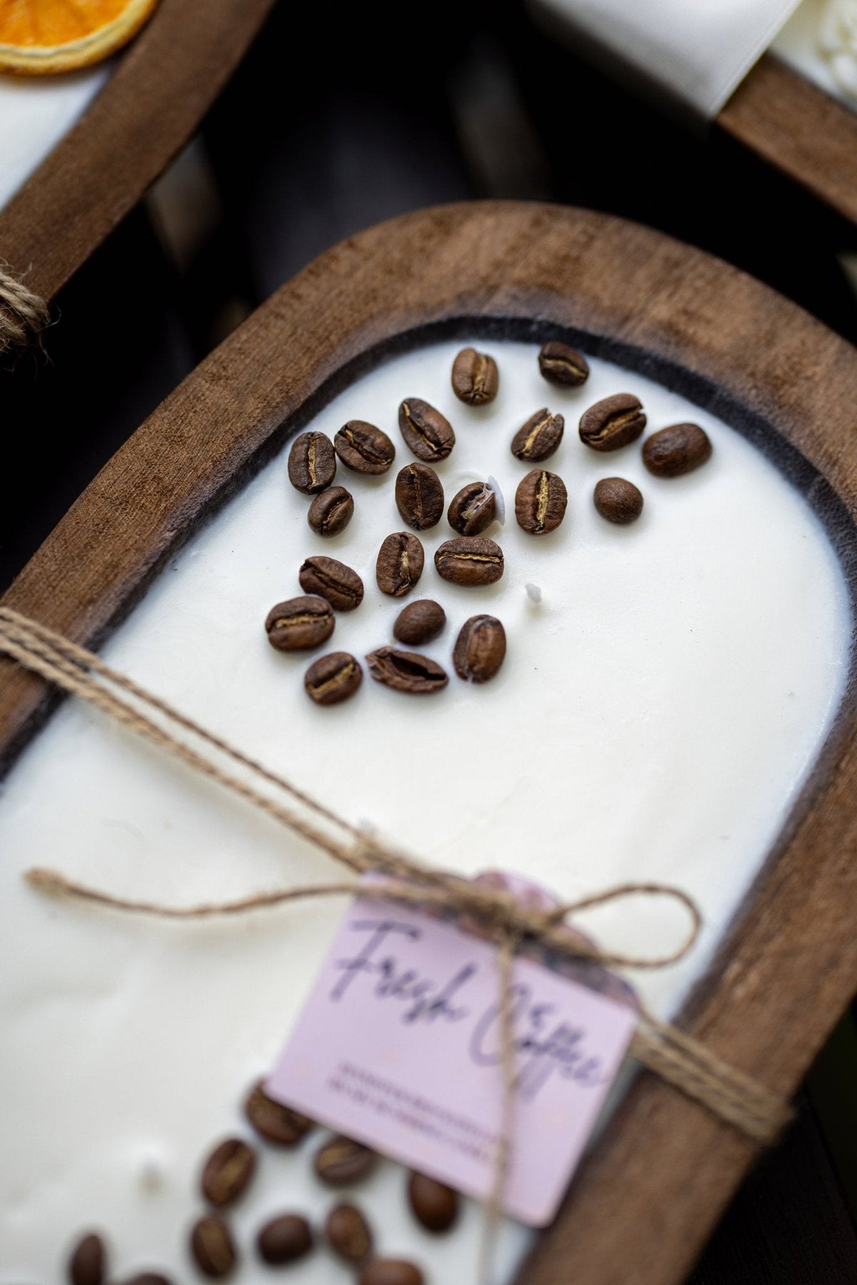 Top view of coffee-scented candle in wooden bowl with coffee beans and tied tag