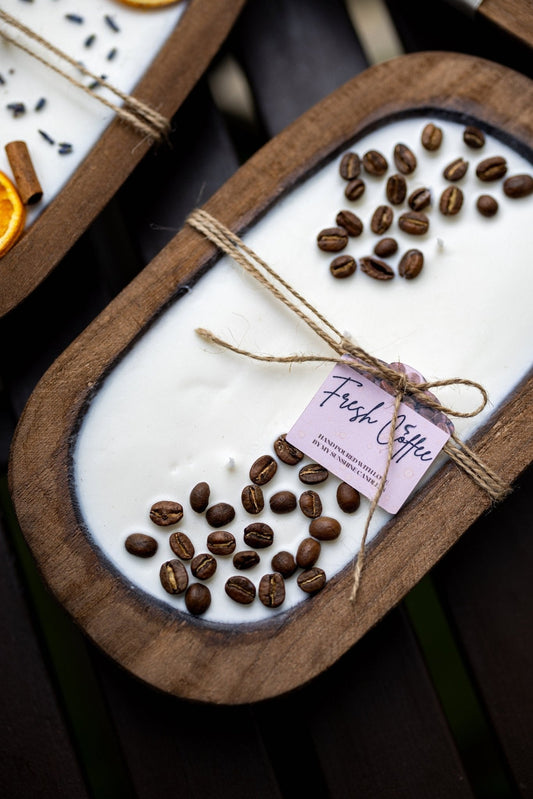 Coffee-scented candle in oval wooden bowl with scattered coffee beans and tied label