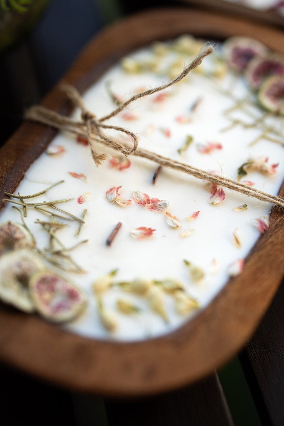 Wood dough bowl candle close view: white wax with dried flowers, herbs, and fig slices