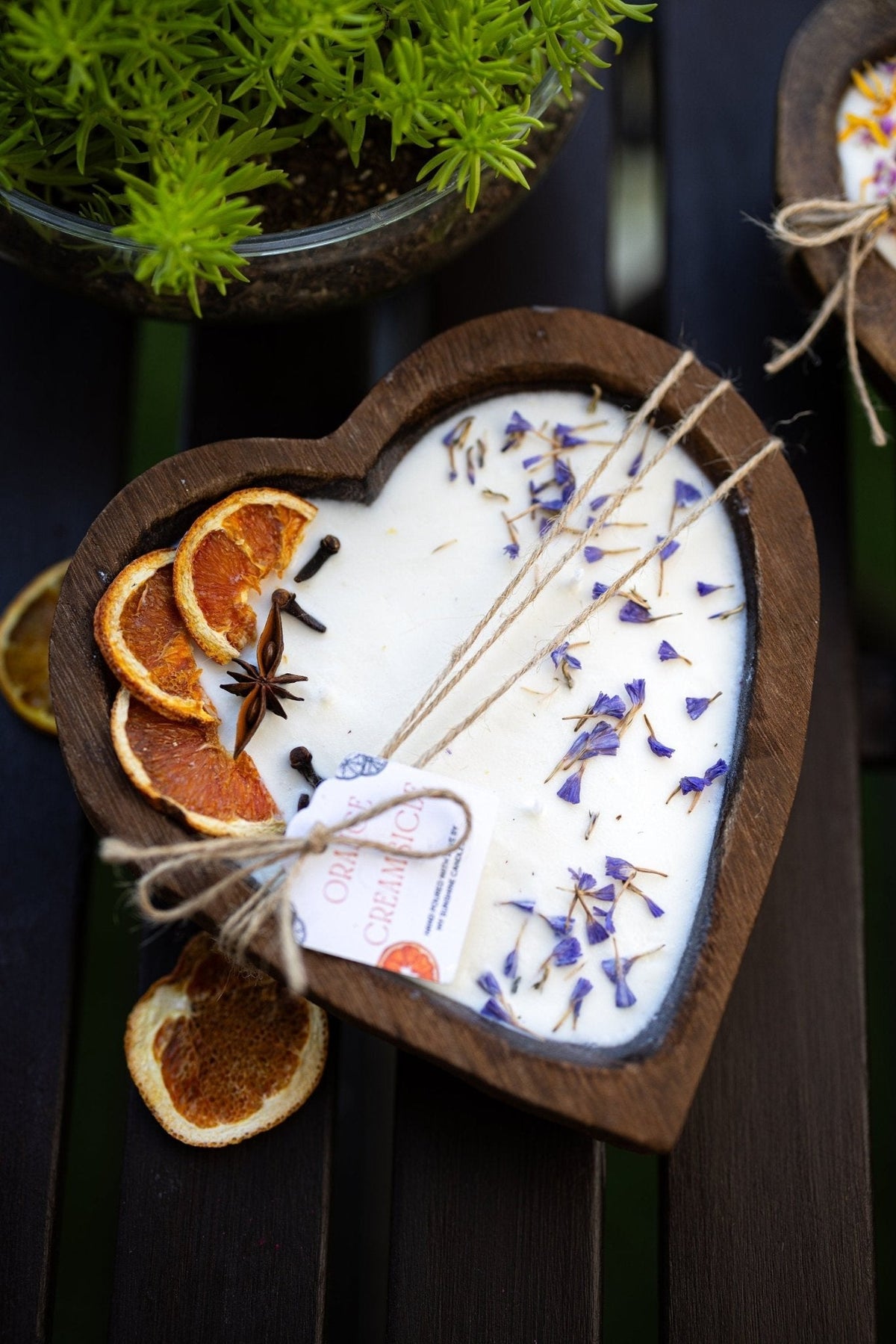 Heart-shaped white soy candle in dark wood holder with 3 cotton wicks and blue sprigs