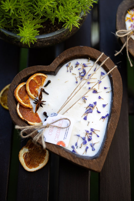Heart-shaped white soy candle in dark wood holder with 3 cotton wicks and blue sprigs