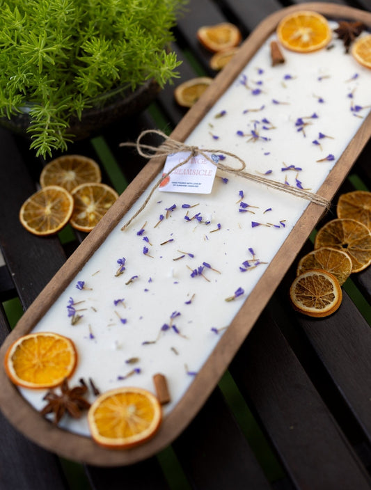 Hand-carved wooden dough bowl candle with white wax, orange slices, and blue lavender sprigs, unlit