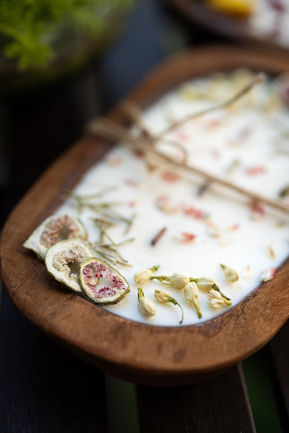 Wood dough bowl candle close-up of white wax with dried botanicals and twine tie wick