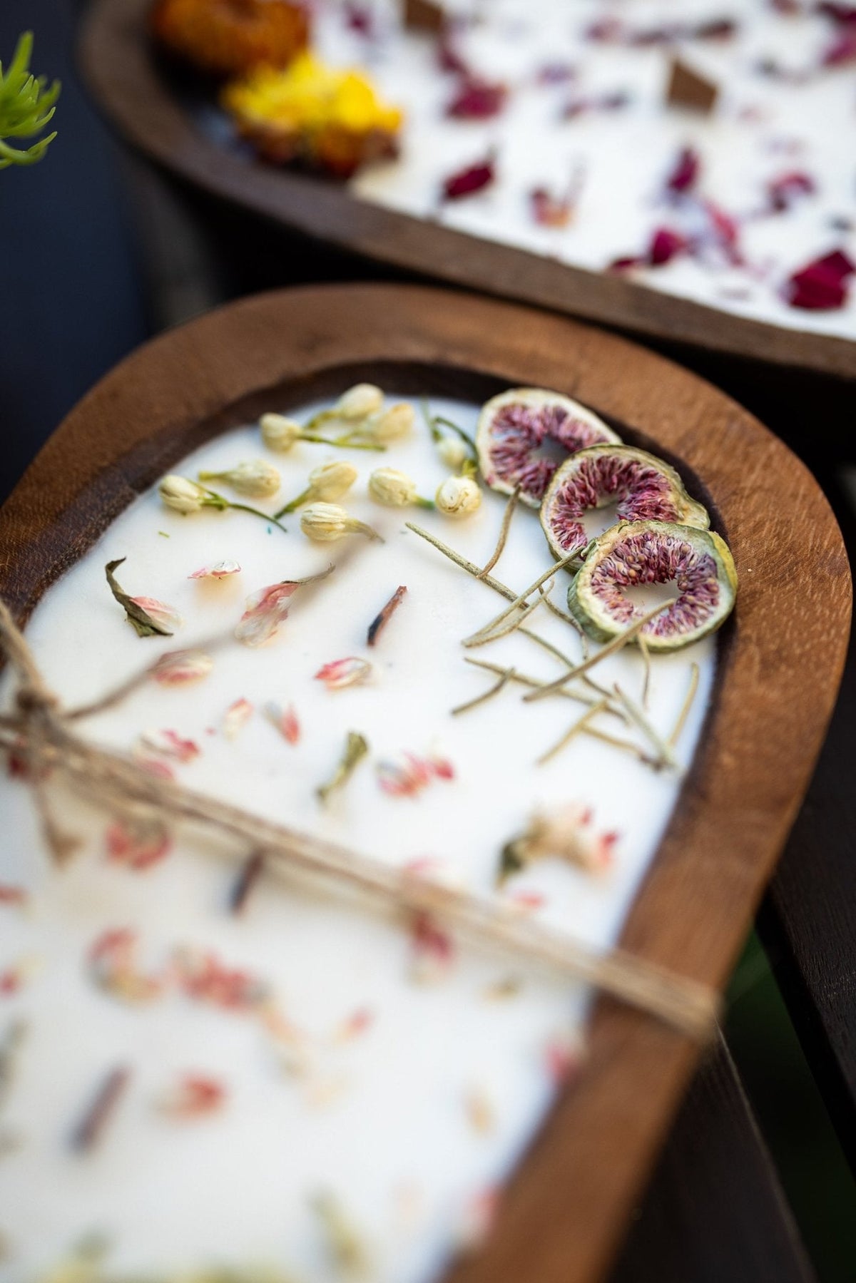 Wood dough bowl candle showing white wax topped with fig slices and dried stems