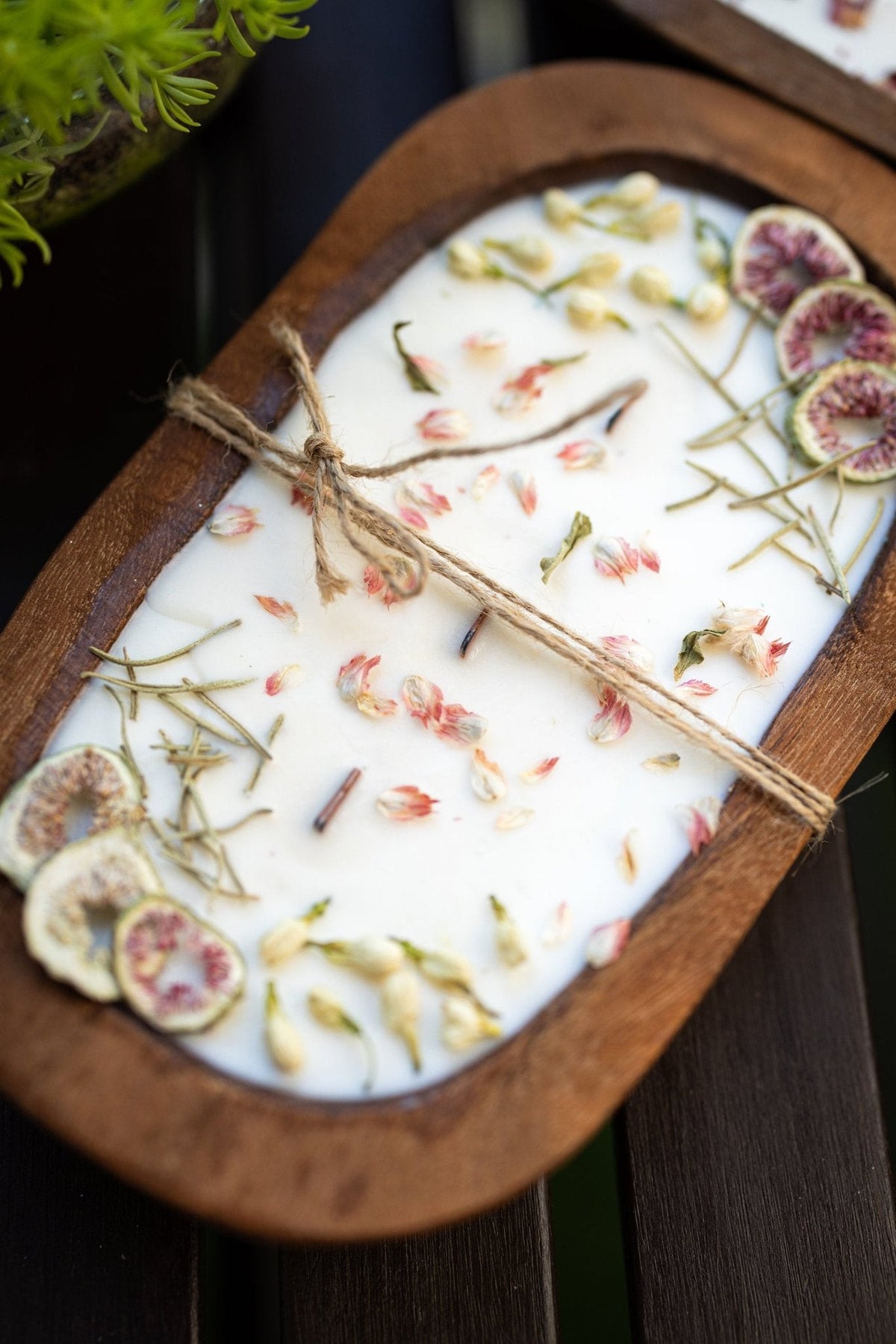 Wood dough bowl candle detail: white wax with dried herbs, small flowers, and fig slices