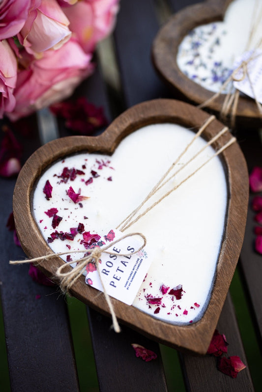 Heart-shaped wooden candle bowl with white wax, rose petals, and twine-wrapped rose label