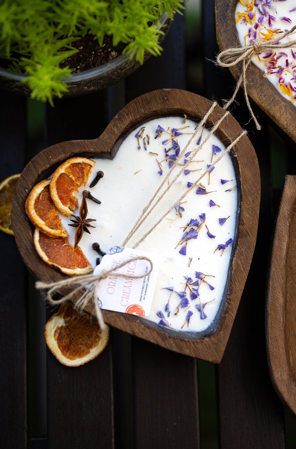 Heart-shaped white soy candle in wooden tray with blue sprigs, orange slices, and 3 wicks