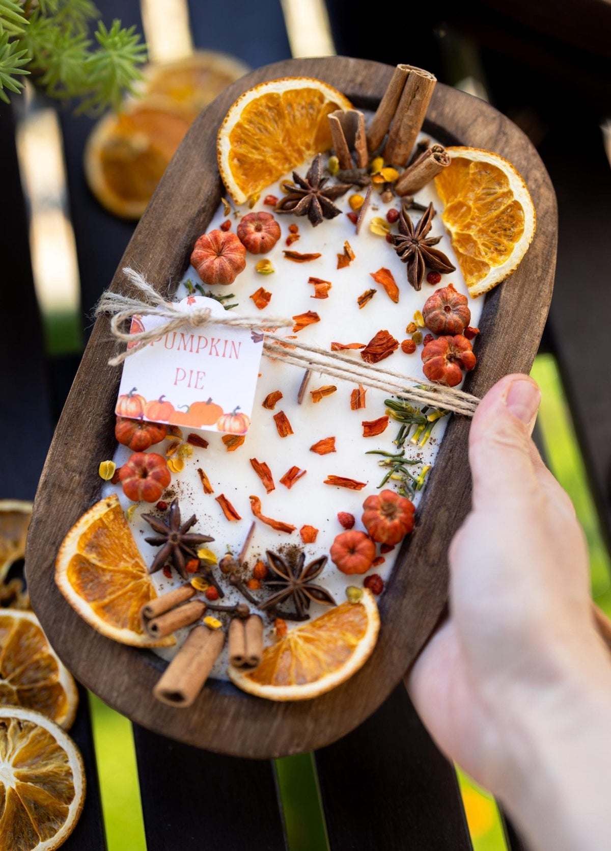 Large wooden candle bowl with pumpkin spice wax, dried orange slices, star anise, hand holding