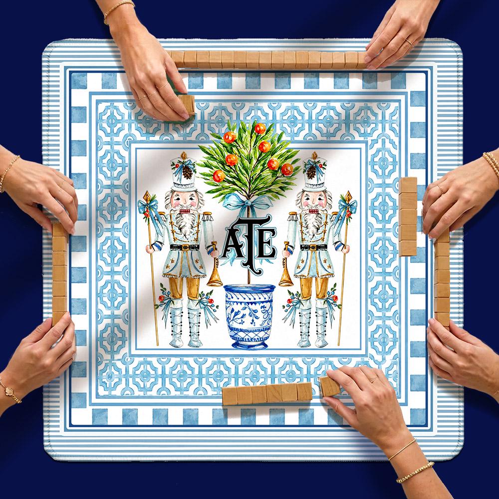 Holiday mahjong mat with a blue patterned border, nutcrackers, a decorated tree and custom initials, in use.