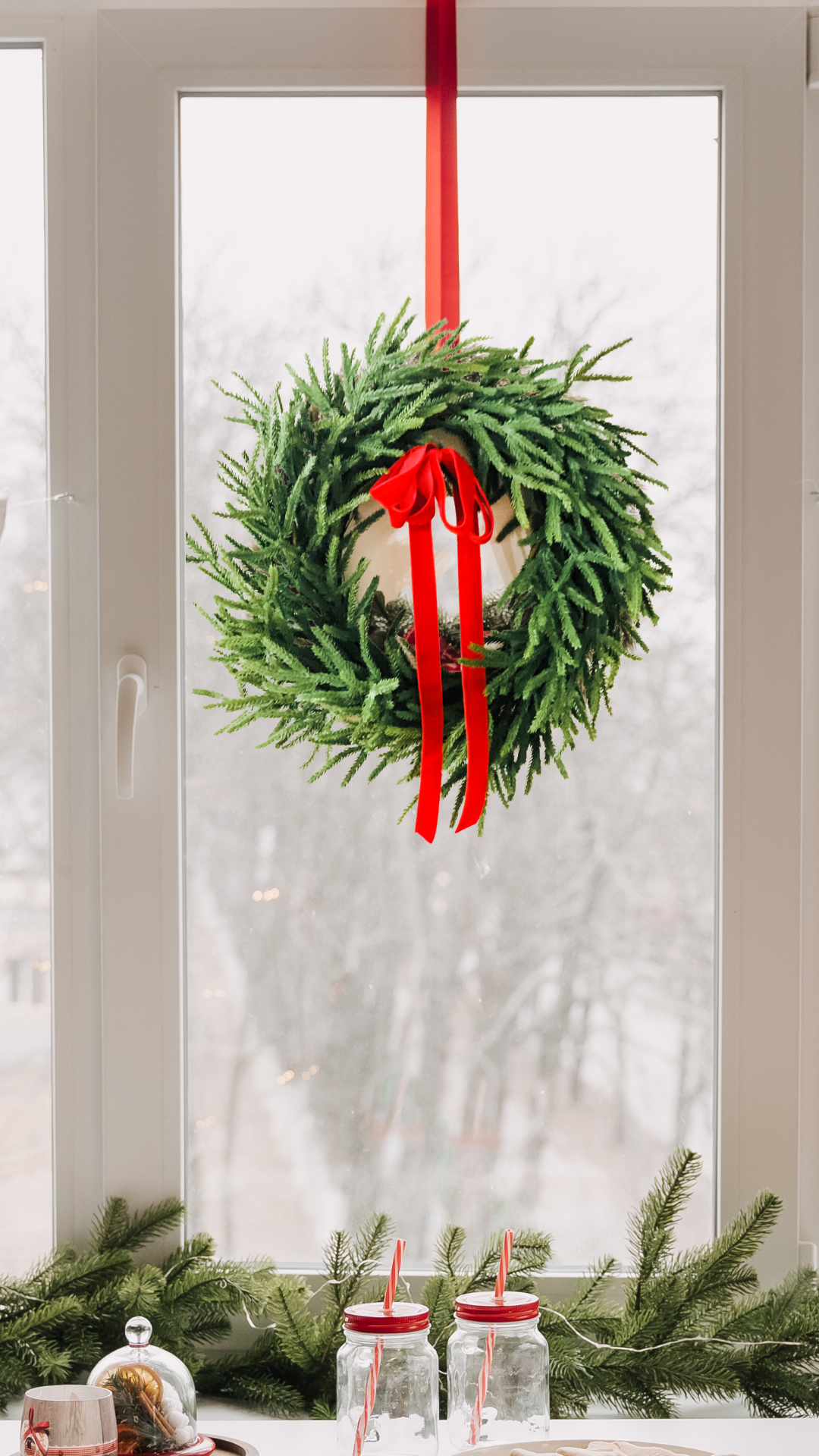 Norfolk pine wreath with red ribbon hanging on a white door