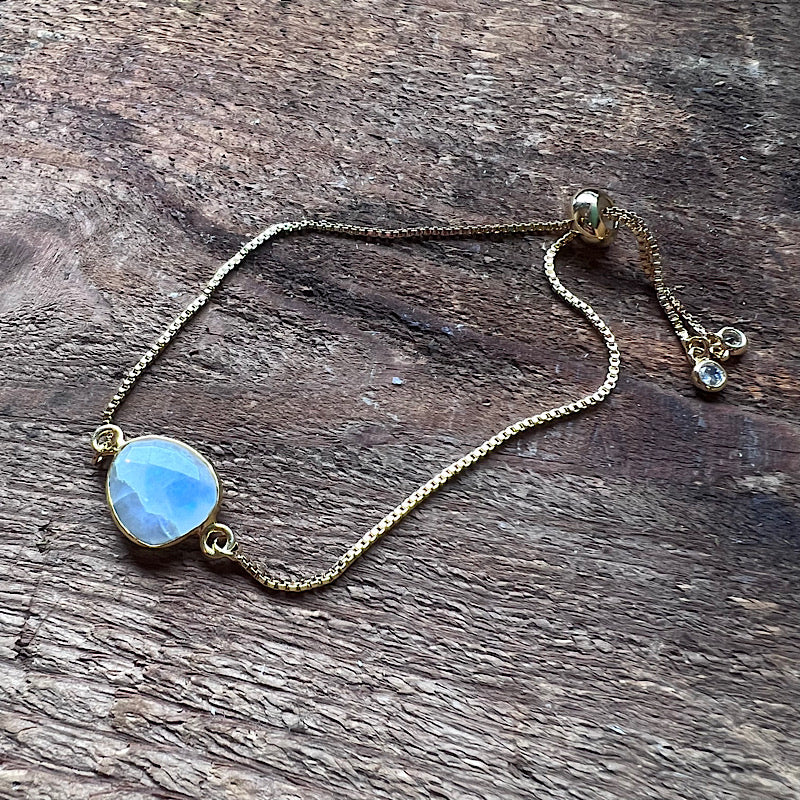 Gold-tone adjustable bracelet with round blue moonstone and small dangling gem