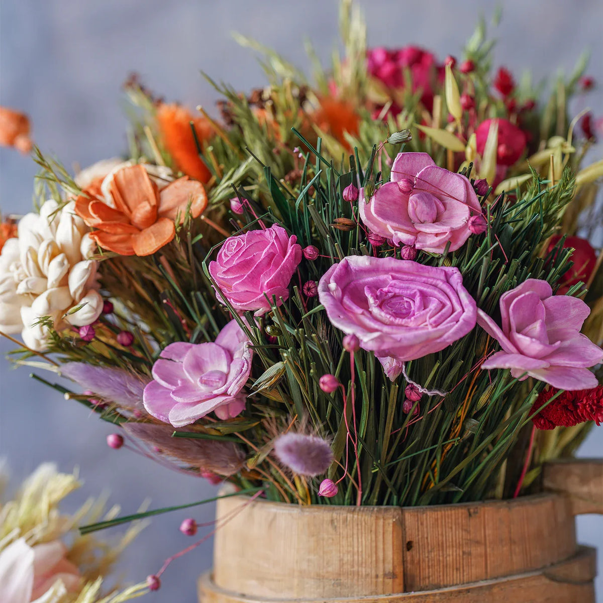 Dried floral bouquet with pink roses, purple petals, and green grasses in a wooden pot