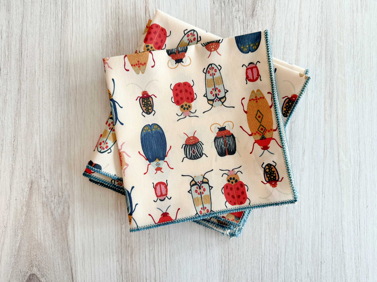 Beetle-print cloth napkins with blue trim, folded square set