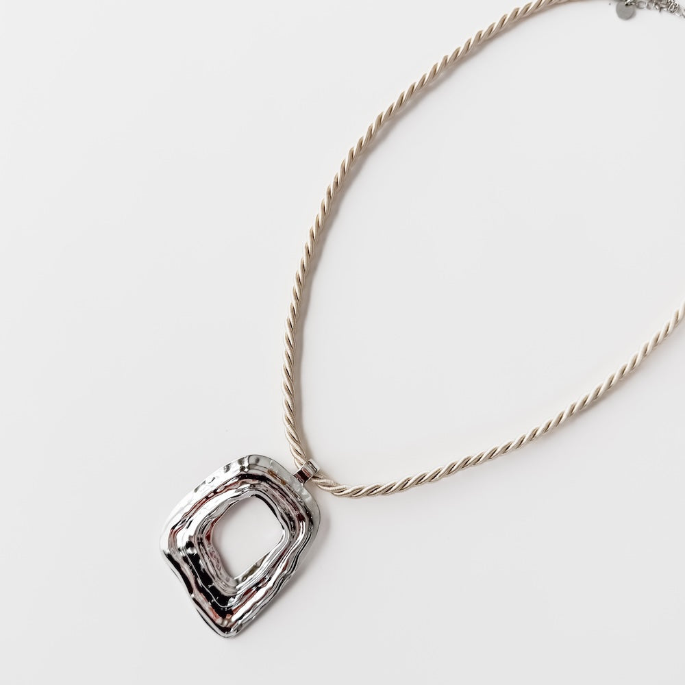 Close-up of silver-tone irregular square statement pendant on a twisted chain