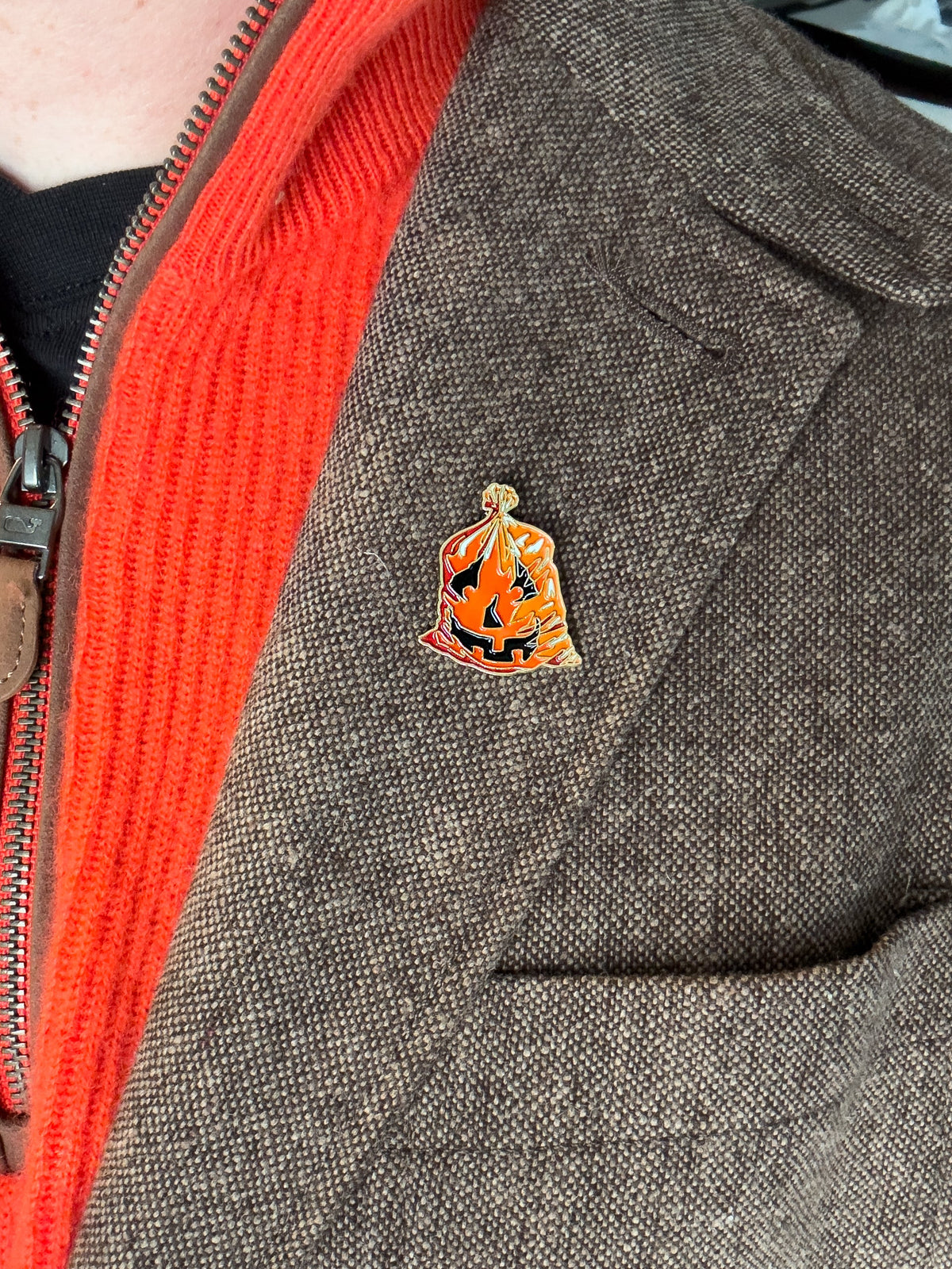 Enamel leaf-bag pumpkin pin on gray jacket, orange and black enamel with gold trim