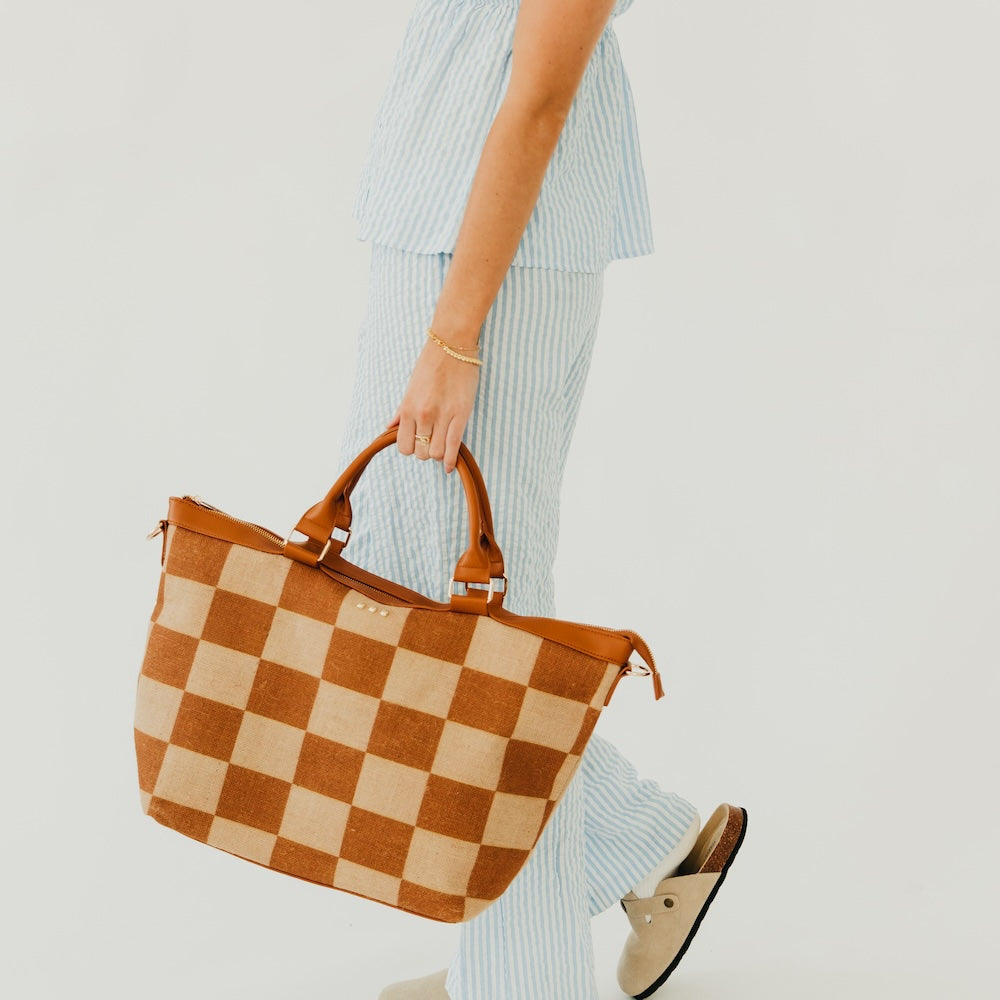 Jute tote bag with tan and brown checkered print, carried by top handles, side view