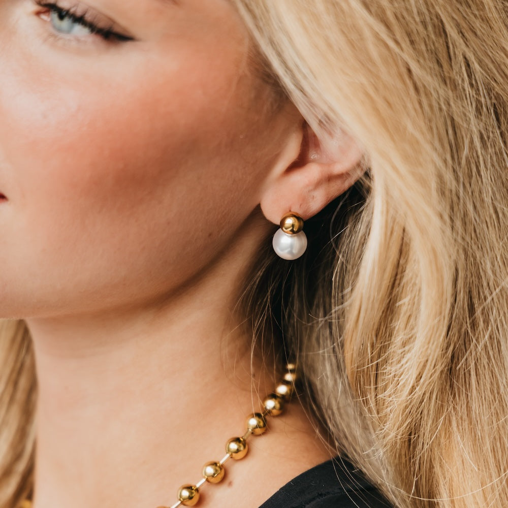 Gold-tone pearl drop earrings with small bead accents, worn on ear
