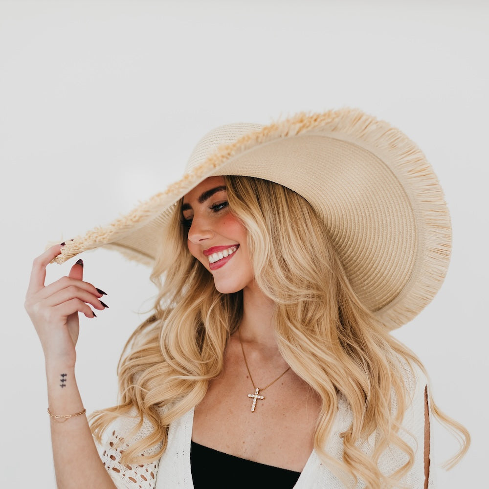 Wide light beige sun hat with textured weave and fringe along the brim
