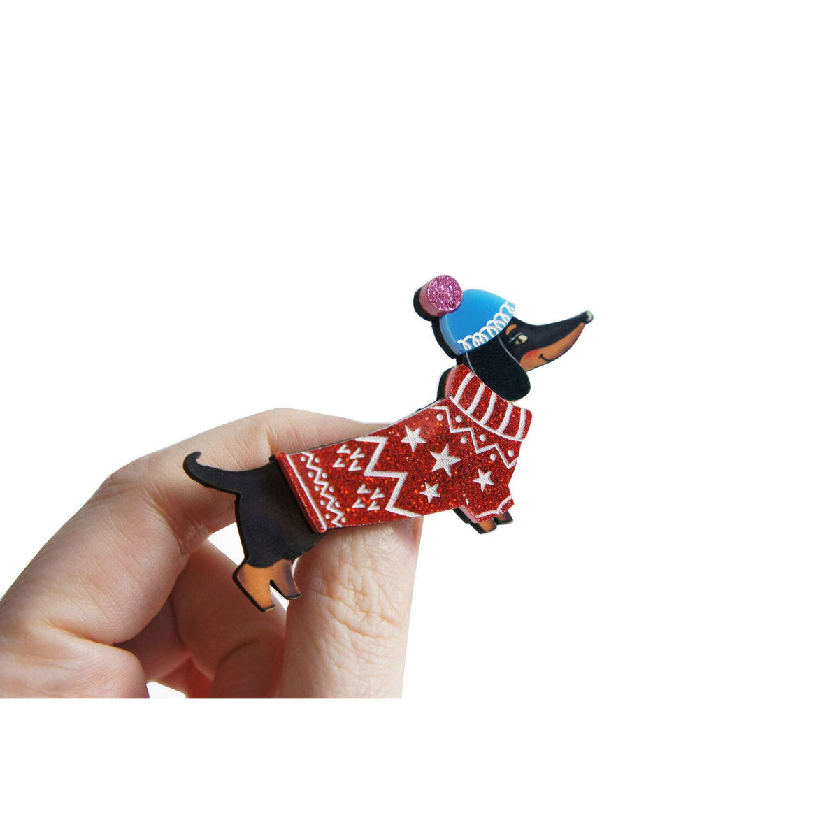 Dog brooch in hand: black dachshund with red patterned stars sweater and blue hat
