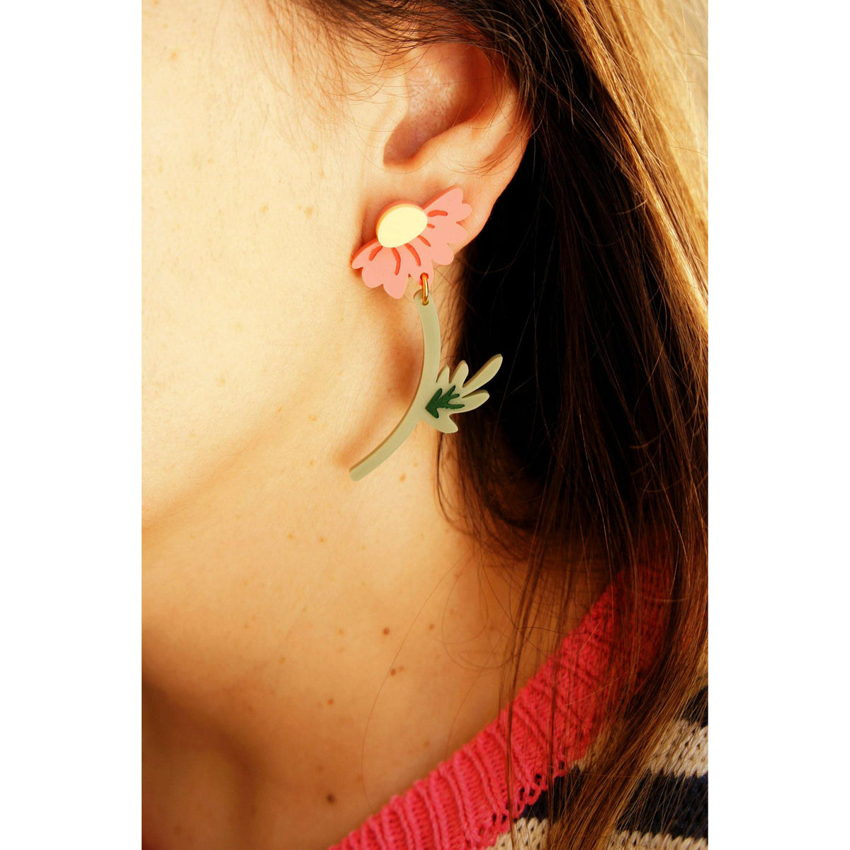 Pink flower earrings with yellow centers and green leaf details on ear