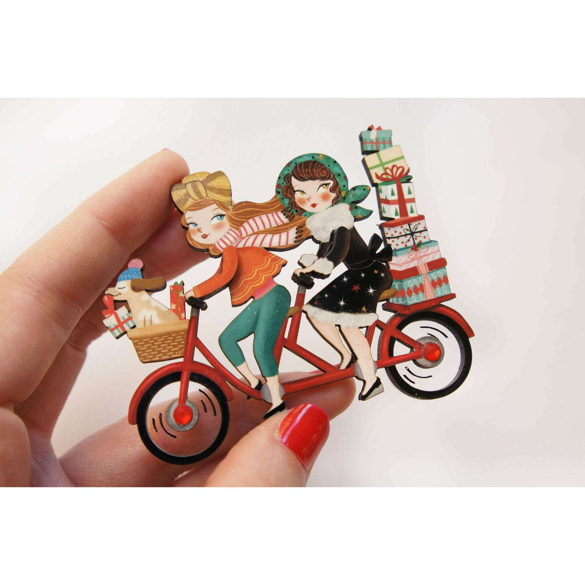 Bicycle enamel brooch held in hand, two riders and stacked gift boxes