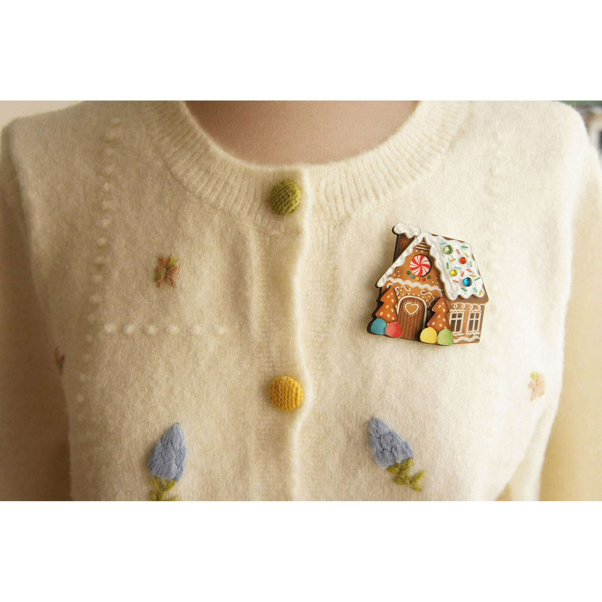 Gingerbread house brooch pin on cream sweater, colorful enamel house with red door