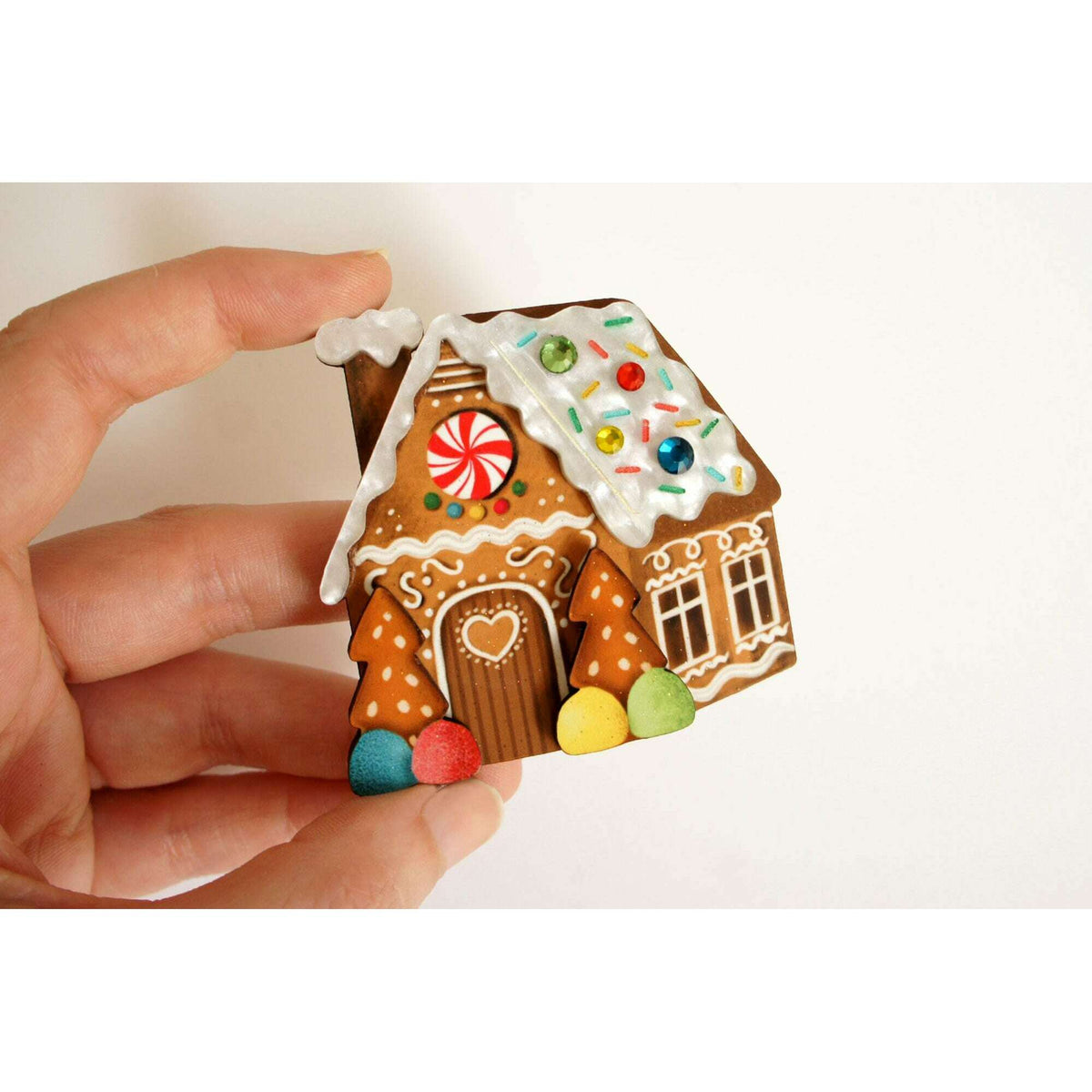 Gingerbread house enamel brooch in hand, decorated roof and candy accents with windows
