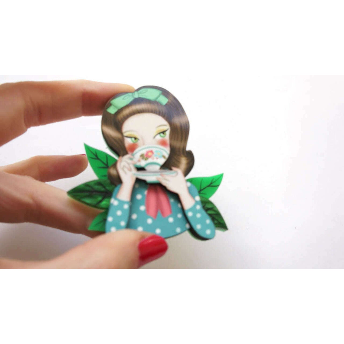Girl tea-drinking brooch held by fingers, front with blue polka dress