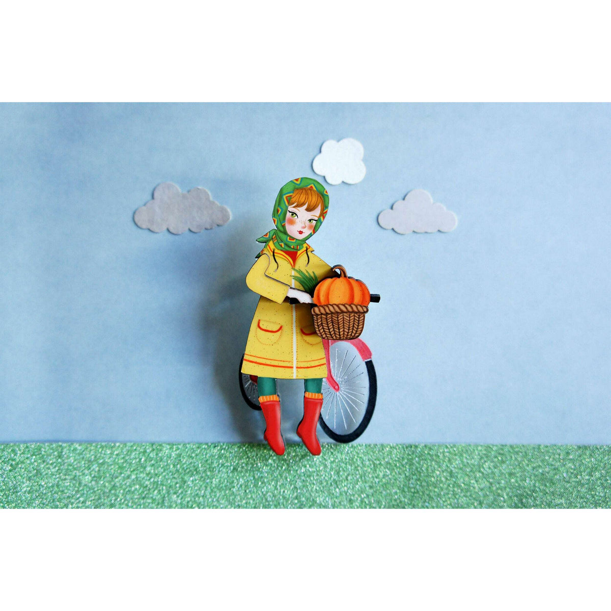 Bicycle girl brooch figurine of hooded child carrying orange pumpkins in wicker basket