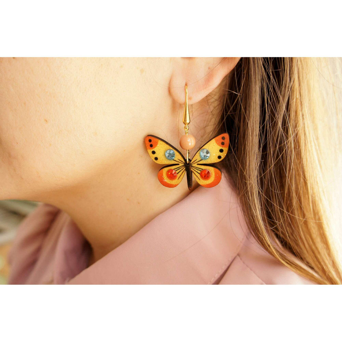 Multicolor butterfly drop earrings shown on model ear, gold hook and bead charm