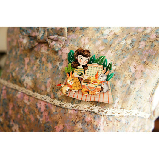 Picnic enamel brooch with cartoon girl holding basket, rabbit beside, plaid blanket