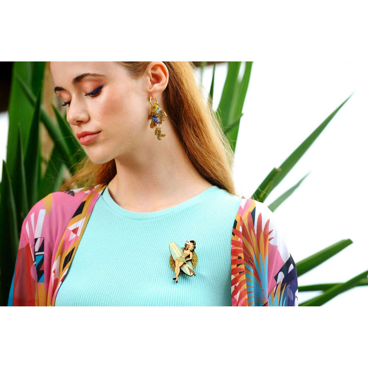 Surfer girl brooch worn on a light blue top; small glitter figure with surfboard