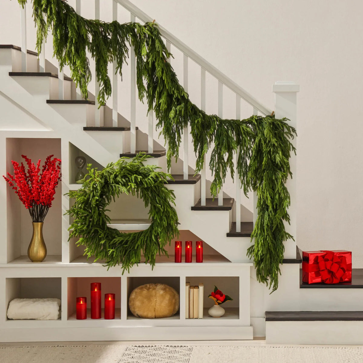 Green faux pine wreath hanging on a stair rail, with long trailing branches.