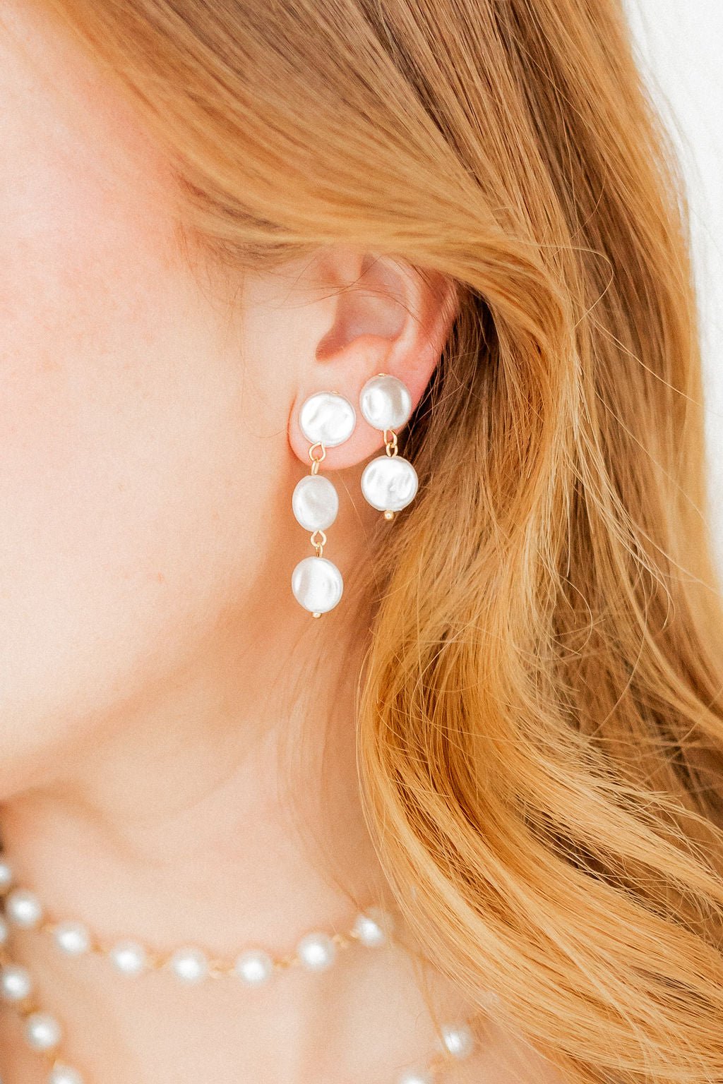 Close-up: pearl drop earrings with three white pearl discs and gold hooks