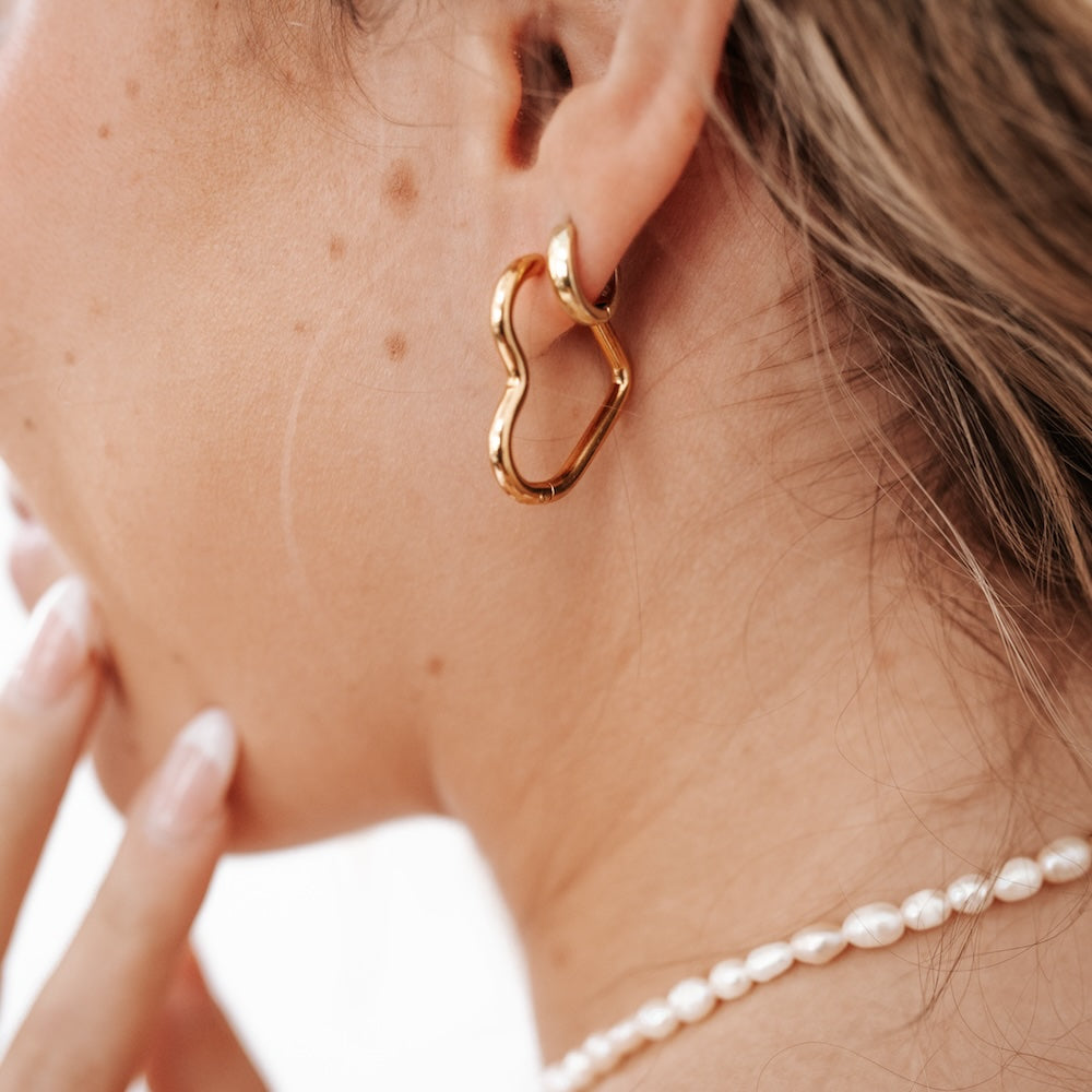 Gold-tone heart hoop earrings with hinged closure and open heart outline.