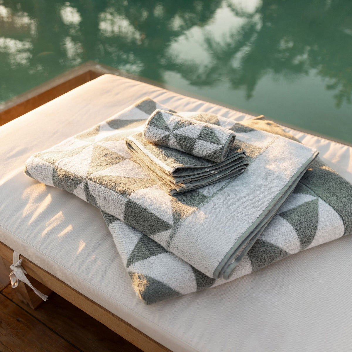 Folded sage and ecru geometric cotton towels with triangle pattern, stacked on a lounge bed.