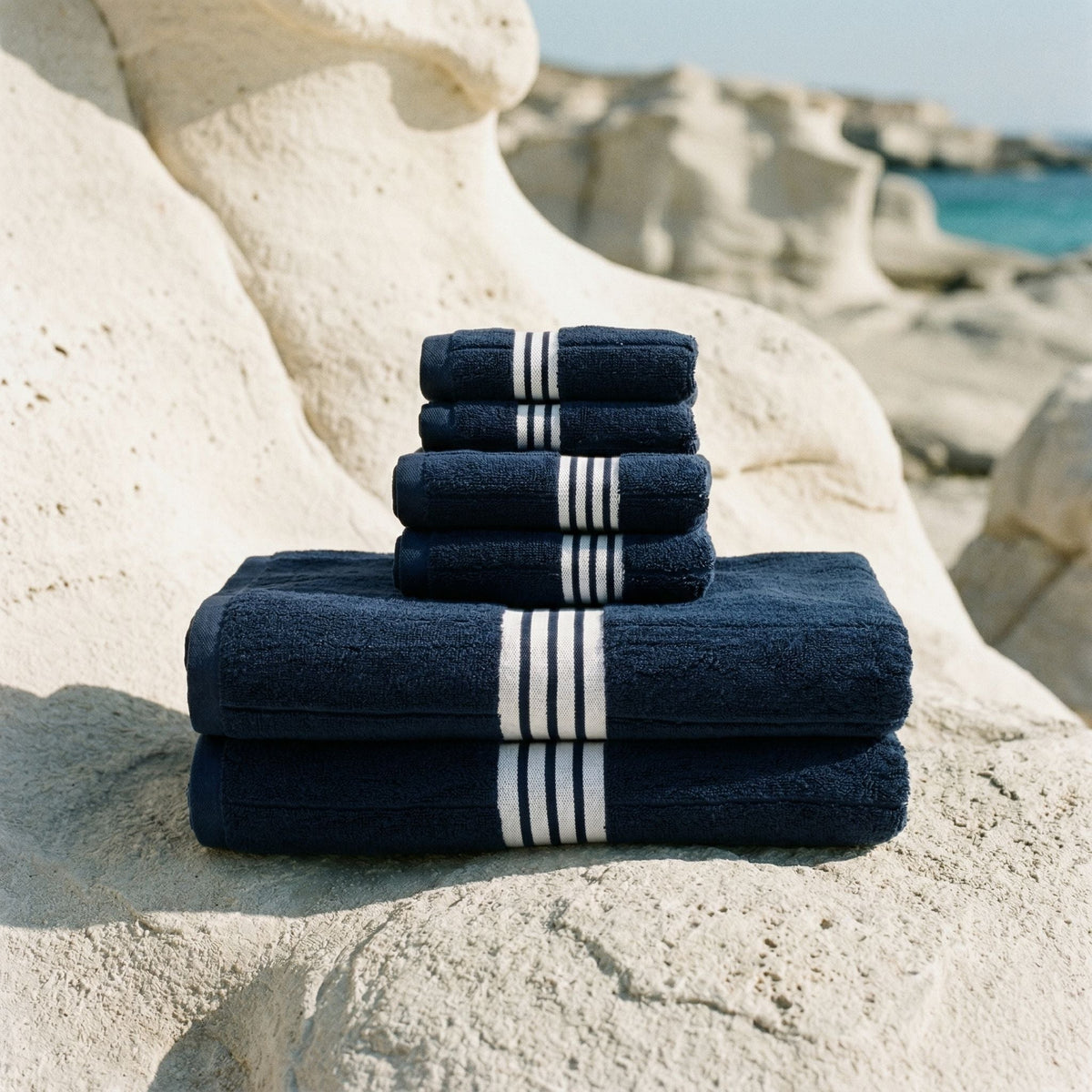 Dark navy cotton towels with white striped bands, stacked on stone