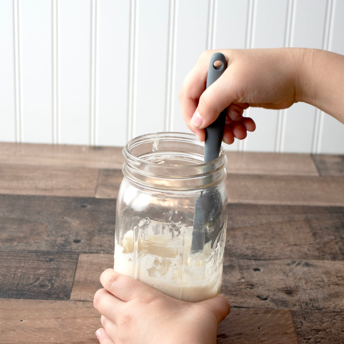 Hands lifting a gray silicone jar scraper from a clear jar