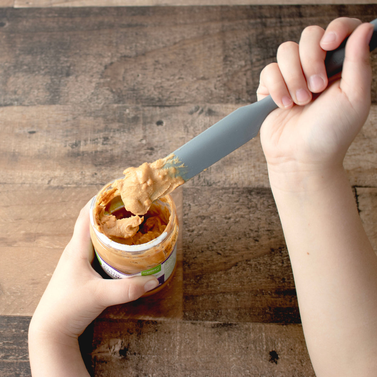 Gray silicone jar scraper in hand spreading creamy paste from a jar