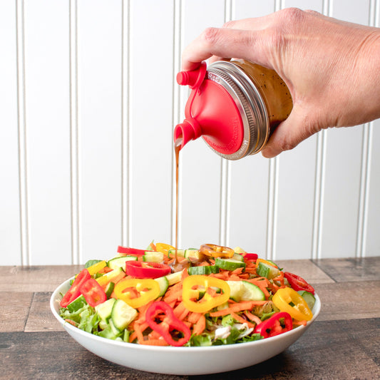 Red silicone oil pour lid and mason jar band, pouring a thin stream of oil
