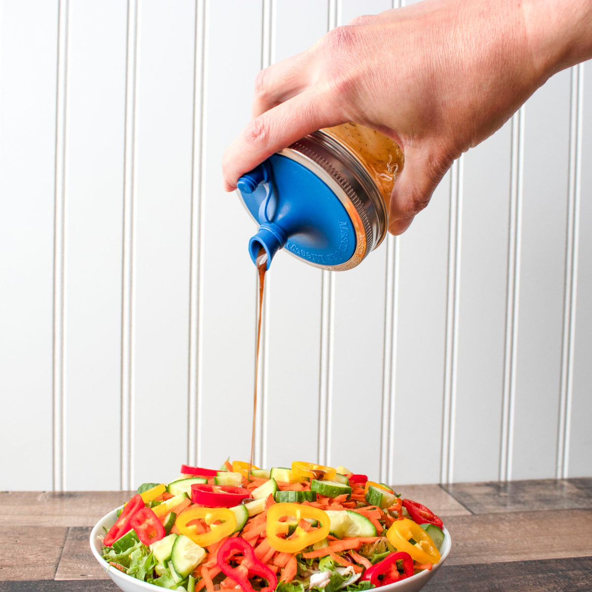 Blue silicone oil pour lid on mason jar band, pouring a thin stream of oil