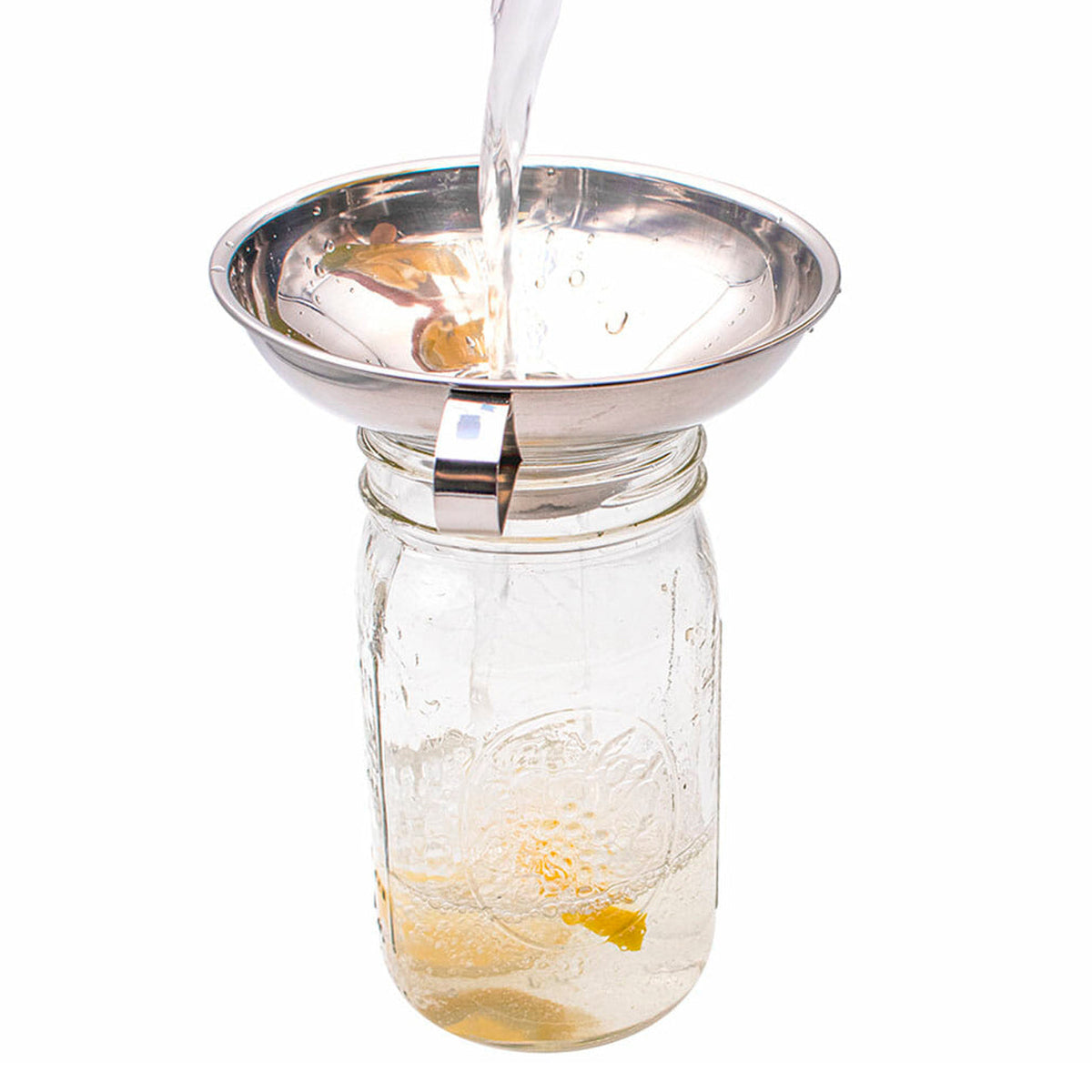 Stainless steel canning funnel receiving clear liquid pour into mason jar