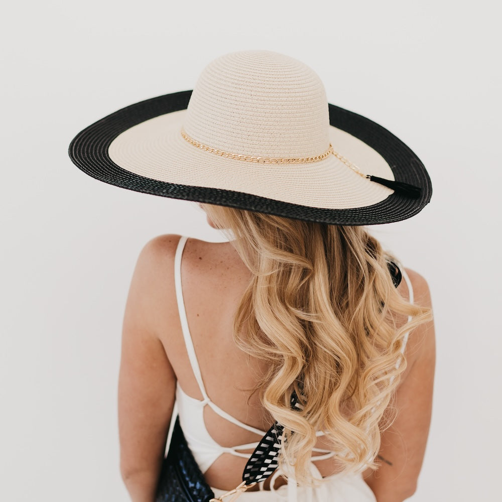 Wide floppy sun hat, tan crown with black brim and gold chain trim, worn from back